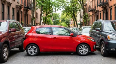 Compact car rental parallel parked on a busy street in New York surrounded by tall buildings