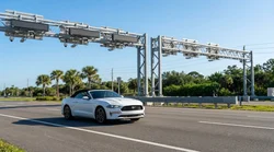 White car rental passing under an electronic toll gantry on a sunny Florida highway