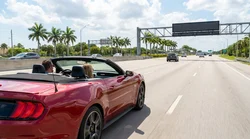 White car rental passing under an I-4 Express toll gantry on a sunny highway in Orlando
