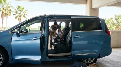 Parent securing a child seat inside a car rental parked under palm trees in Florida