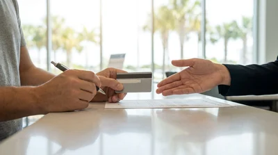 Close-up of a customer handing a credit card to an agent at a bright car hire counter in Florida