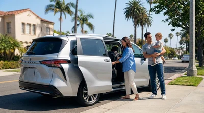 Parent buckling a toddler into a car seat inside a car rental parked along a sunny California beach