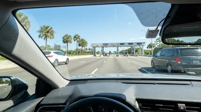 White car rental passing under an electronic toll gantry on a sunny Florida highway
