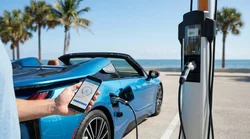 Person using a smartphone next to a plugged-in electric car rental at a sunny Florida charging station