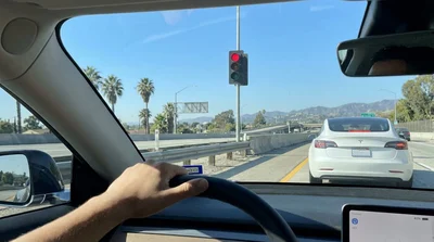 A car hire stopped at a red ramp metering light on a busy freeway on-ramp in Los Angeles