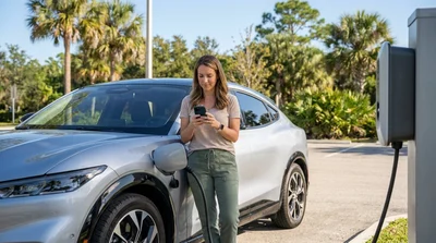 Person plugging a charging cable into a modern electric car rental parked under sunny palm trees in Florida