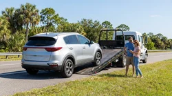 Tow truck lifting a damaged car rental vehicle on a sunny Florida highway