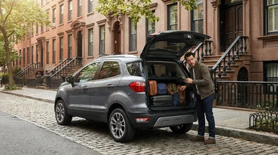 Person loading a suitcase into the trunk of a car rental on a New York street