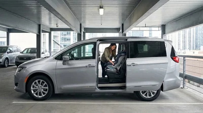 Parent buckling a child into a safety seat inside a car rental parked on a New York street