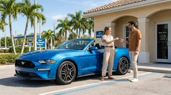 Two people driving a car rental along a sunny coastal road lined with palm trees in Florida