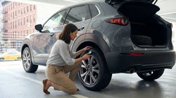Person crouching to inspect the front tire of a car rental parked on a New York street