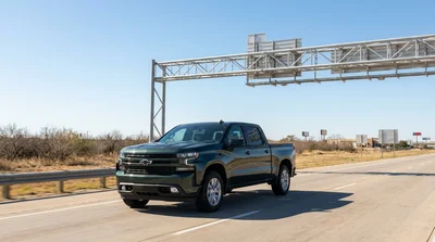 Silver car hire driving under an electronic toll gantry on a sunny Texas highway