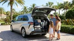 Suitcases packed in the open trunk of a minivan car rental near a sunny Florida beach