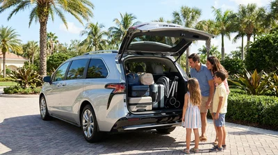 Suitcases packed in the open trunk of a minivan car rental near a sunny Florida beach