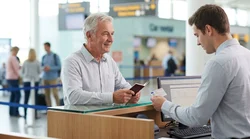 Older man handing identification documents to a clerk at a car rental counter in the United Estates