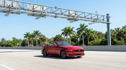 White car rental driving through a sunlit electronic toll booth on a Florida highway