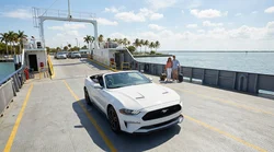 White car hire parked on the open deck of a ferry crossing a sunny Florida bay