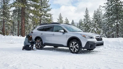 Silver car rental with snow chains on its tires driving along a snowy mountain highway in California