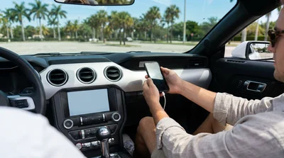 Driver plugging a smartphone into a dashboard screen inside a car rental on a sunny Miami street