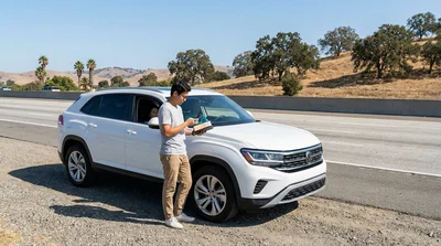 White SUV car hire driving along a scenic coastal highway in California next to the ocean