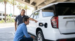Person pressing a fuel grade button on a gas pump next to a car hire in California