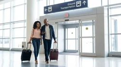 Traveler walking with luggage outside Newark Terminal B in New York toward a car rental shuttle