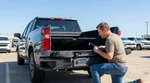 Person inspecting a spare tyre kit in the open trunk of a car rental parked on a sunny road in Texas