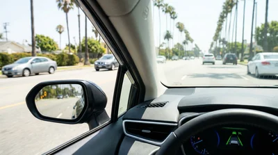 Dashboard and side mirror view from inside a modern car rental driving on a sunny Los Angeles highway