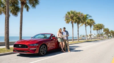 White car rental driving on a sunny coastal road lined with palm trees in Florida