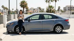 Driver holding a smartphone showing a parking app inside a car rental on a sunny Los Angeles street