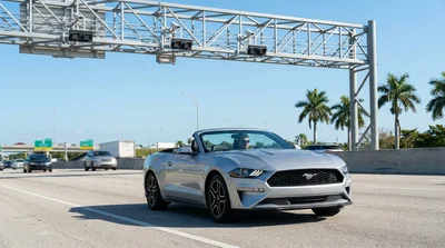 White car rental driving in an express lane under a cashless toll gantry against the sunny Miami skyline