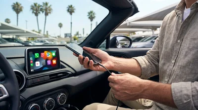 Driver touching an Apple CarPlay dashboard screen inside a car rental parked on a bright Los Angeles street