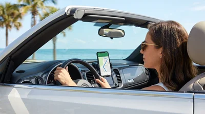Driver using smartphone navigation mounted on the dashboard of a car rental driving on a sunny Florida highway