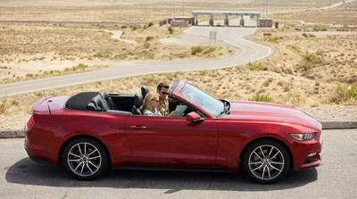 Person driving a modern car rental along a scenic sunlit coastal highway in California