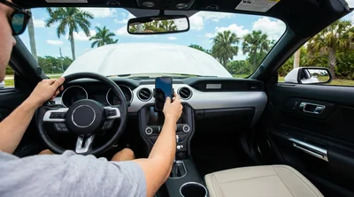 Smartphone displaying GPS in a dashboard mount inside a Florida car rental driving past palm trees
