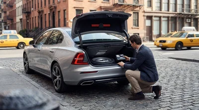 Driver checking the spare tire in the trunk of a car rental parked on a New York street