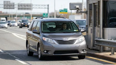 A silver car rental passing through an E-ZPass toll booth in New York