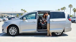 Parent installing a child seat in the back of a car rental parked near a sunny California beach