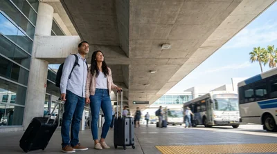 Hola car rental shuttle bus picking up passengers with luggage outside Terminal 6 in Los Angeles