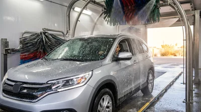 Silver car rental covered in soap and water inside an automatic car wash in Texas