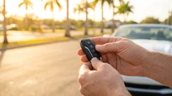 Hand holding a key fob next to a car rental vehicle in a sunny Florida parking lot