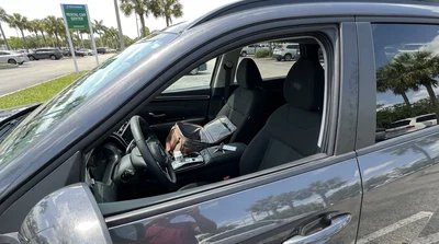 A person driving a white car rental along a sunny coastal highway in Florida