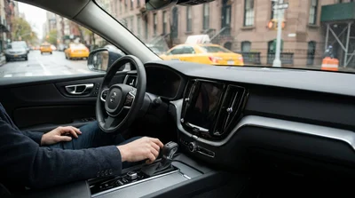 Driver steering an automatic car rental down a busy New York avenue lined with tall skyscrapers