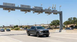 Silver car rental driving under an electronic toll camera on a Texas highway