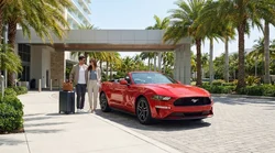 Red convertible car rental driving along a sunny palm-lined coastal road in Miami