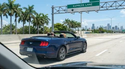 A white car rental passing an I-95 express lane toll sign on a highway in Miami