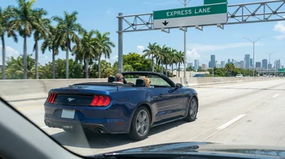 A white car rental passing an I-95 express lane toll sign on a highway in Miami