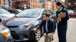 Person inspecting scratches on a car rental bumper and holding a clipboard in New York