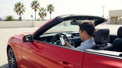 Woman holding a smartphone next to a parked car rental on a palm-lined street in Los Angeles