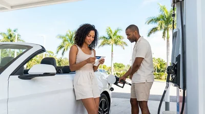 Close-up of a person pumping gas into a white car hire at a bright Miami gas station